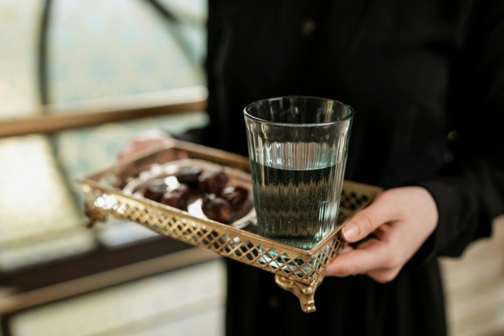 A glass of water and dates on a decorative tray held indoors.