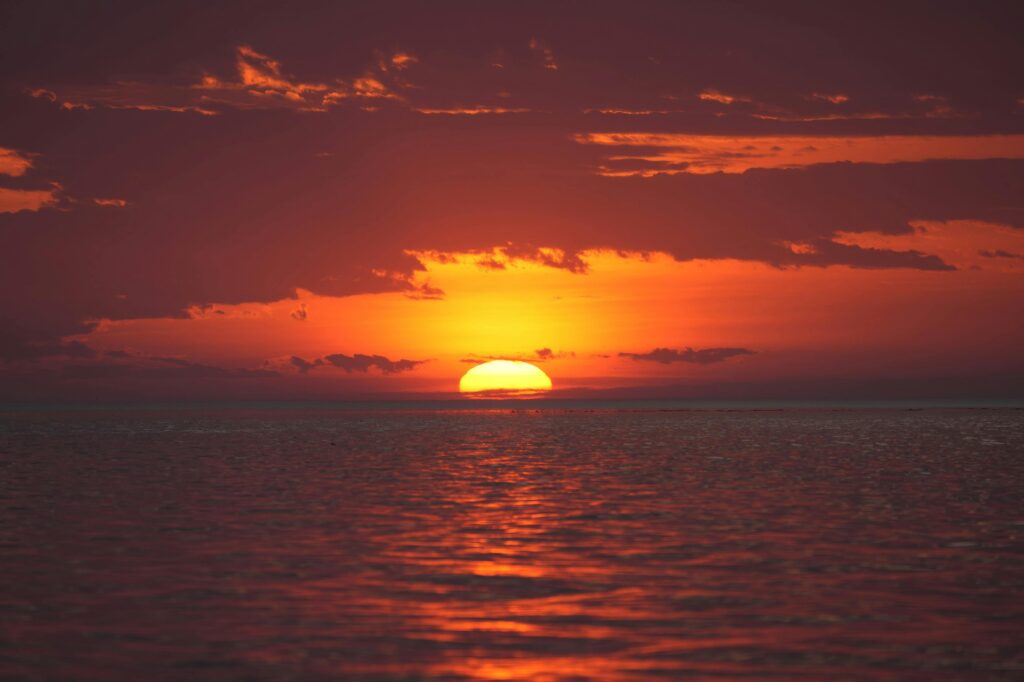 A breathtaking sunset over the ocean with vivid red and orange hues reflecting on the water.